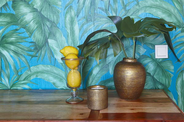 Beberapa lemon di atas meja kayu dengan vas bunga dan latar belakang motif daun tropis.