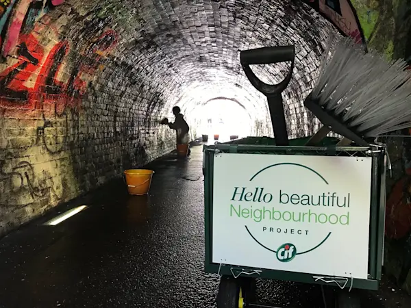 Un túnel con grafitis y una persona limpiando, junto a un carro de limpieza con el letrero