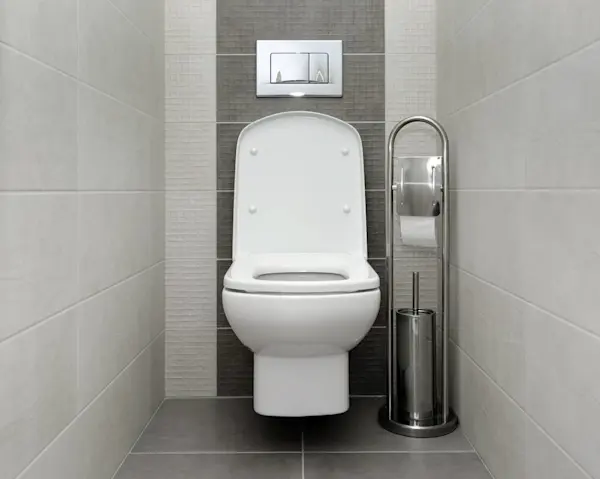 Toilet bersih dengan dudukan tutup tertutup dan tempat tisu di sampingnya di dalam kamar mandi berdinding ubin.