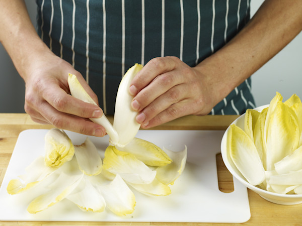 Person peeling and separating leaves of endive on a cutting board.