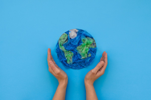 Twee handen houden een bol gemaakt van gerecyclede plastic zakken tegen een blauwe achtergrond.