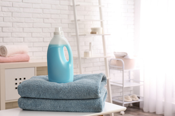 Botol deterjen cair biru di atas handuk biru di ruang laundry.